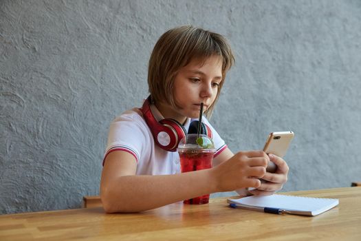 schoolgirl with headphones and red icy lemonade uses smartphone, surfs internet