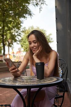 young well dressed asian woman sitting at table with coffee, using smartphone
