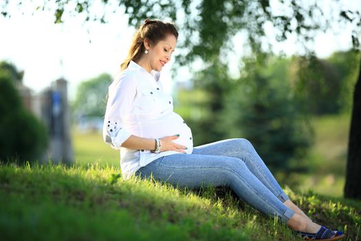 expectant mother sits on the grass in a Park on a Sunny day.
