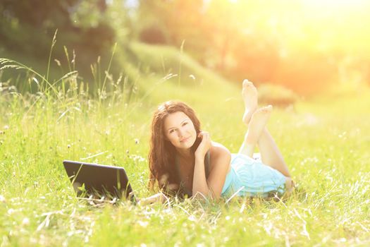 Beauty girl with laptop outdoors in a park on a sunny day
