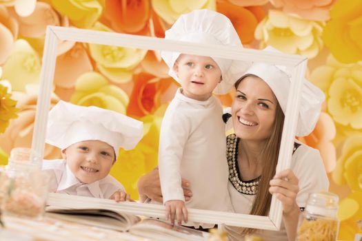 Happy mother and her children in the form of a chef holding a frame and create the illusion of painting