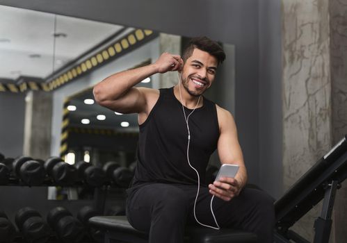 Smilling man using smartphone with earphones in gym