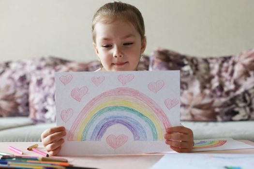 Girl painting rainbow at home, a symbol of UK National Health Service (NHS). Thanks to the doctors for their work. Stay at home Social media campaign.