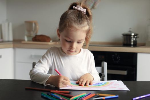 Girl painting rainbow at home, a symbol of UK National Health Service (NHS). Thanks to the doctors for their work. Stay at home Social media campaign.