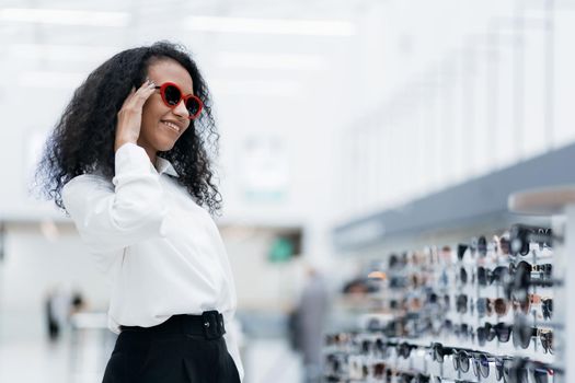 happy young woman in new sunglasses standing in the optics department .