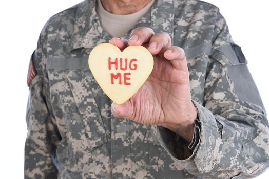 Closeup of a soldier holding a Heart Shaped Valentines Day cookie with the words Hug Me written in red icing. 
