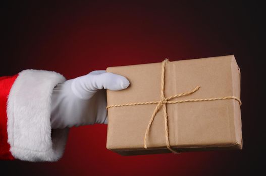 Santa Claus holding a parcel tied with twine over a light to dark red background. Horizontal format showing hand and arm only.