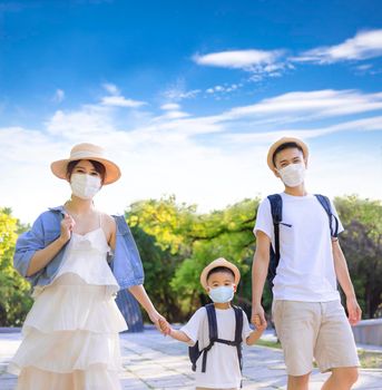 Happy family wearing the medical mask and walking in the park. Family vacations during coronavirus covid-19 pandemic.