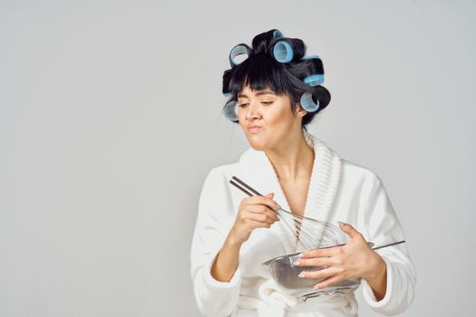 Woman in a white robe with curlers on her head doing homework in the kitchen