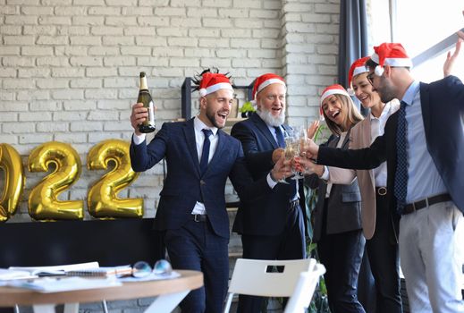 Business people are celebrating holiday in modern office drinking champagne and having fun in coworking. Merry Christmas and Happy New Year 2022.