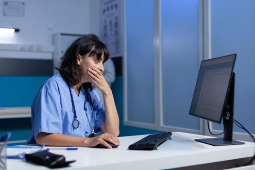 Tired nurse using computer on desk while falling asleep