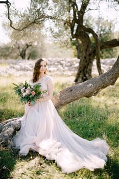 Bride sits on a tree trunk with a bouquet of flowers. High quality photo