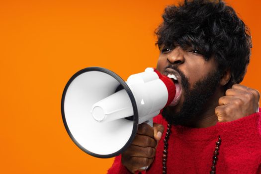 Young african american man in red hoodie screaming in megaphone against yellow background