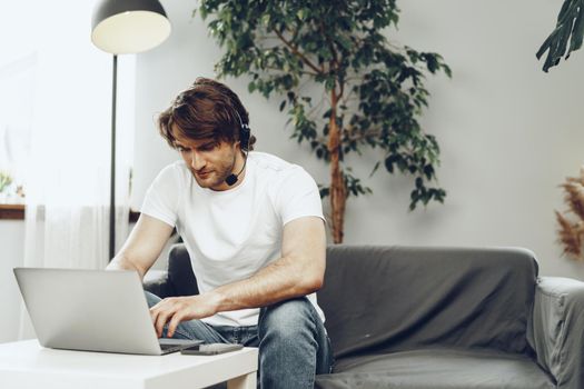 Young man businessman with headset working on laptop from home