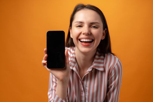 Happy smiling young woman showing you black smartphone screen with copy space