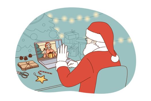 Online Christmas and New year celebration concept. Santa Claus in traditional red costume sitting and congratulating happy child with winter holidays online on laptop during video call distant meting