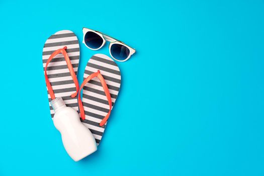 Flip-flops with sunscreen and sunglasses on blue background