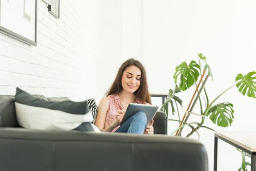 People, interior and leisure concept - happy young woman with tablet pc laying on sofa
