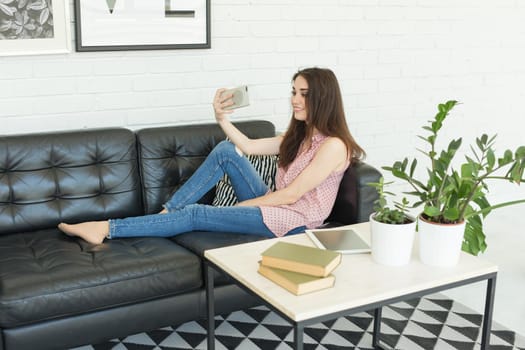 People, technology and photo concept - beautiful brunette taking a selfie with her smartphone at home