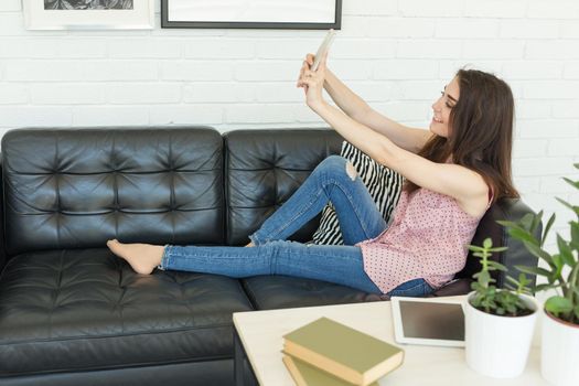 People, blogging and technology concept - young woman taking selfie on sofa