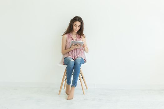 Student, technology and people concept - young woman sitting on chair working with a tablet on white background with copy space