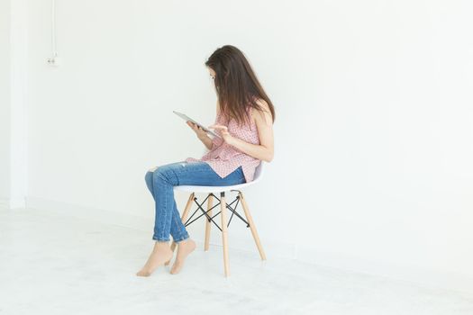 Internet and technology concept - young woman sitting on a chair with digital tablet in white background with copy space