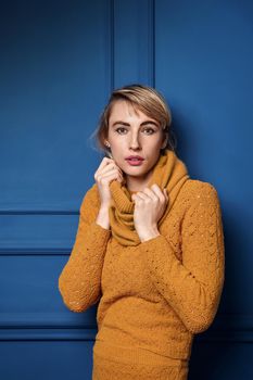 Studio portrait of a young woman in yellow pullover on blue wall background.