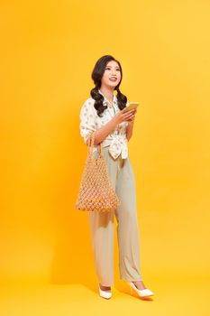 pretty young asian lady looking excited and happy using her phone, carrying a handbag