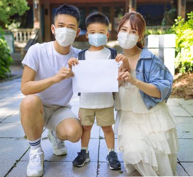 family in medical face mask against coronavirus COVID-2019 holding blank board with information
