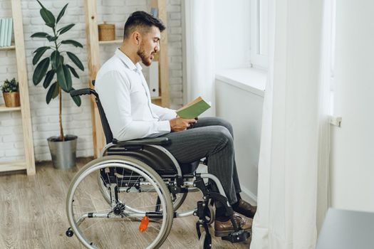 Disabled man in wheelchair reading a book indoors