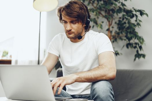 Young man businessman with headset working on laptop from home