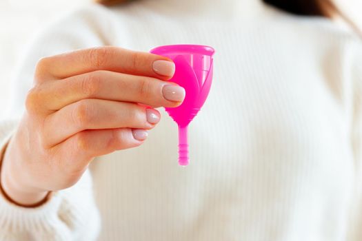 Woman in white sweater holding pink menstrual cup in hands close up