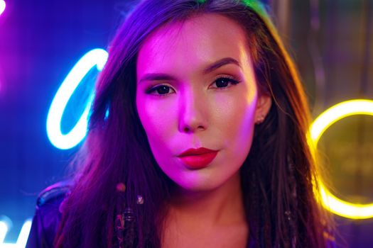 Portrait of a young attractive female standing near neon lamps at night