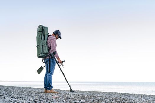 Man with metal detector searching for lost treasures on the beach