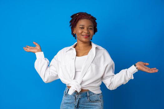 Hesitant african american woman shrugging her shoulders against blue background