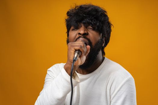 Young bearded african american man singing in microphone against yellow background