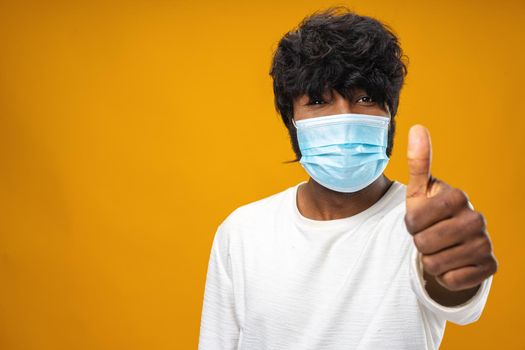 Positive handsome african american man with medical mask against yellow background