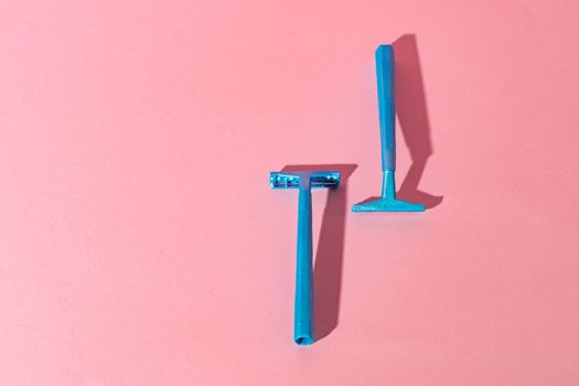 Blue disposable razors on pink paper background