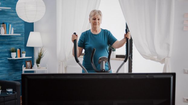 Aged woman using stationary bicycle to do workout training