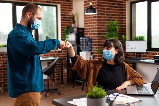 Businessman with medical face mask against covid19 greeting manager woman giving first bump