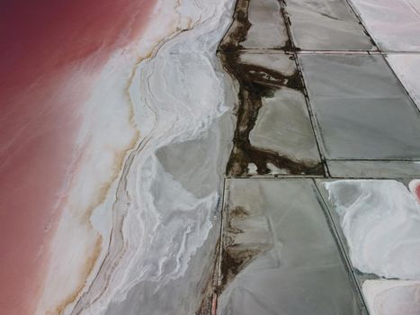 Flying over a pink salt lake. Salt production facilities saline evaporation pond fields in the salty lake. Dunaliella salina impart a red, pink water in mineral lake with dry cristallized salty coast