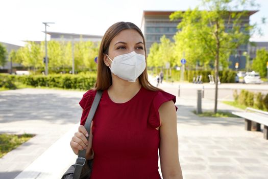 Reflective young woman in empty city street wearing protective mask looking to the side 