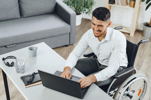 Positive disabled young man in wheelchair working in office