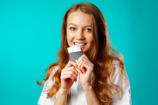 Smiling young woman biting a credit card within temptation of shopping
