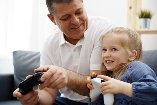 Grandfather and granddaughter playing video games at home.