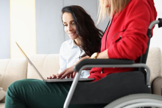 Best friends spend time together watching movie on laptop, woman in wheelchair hold device on lap