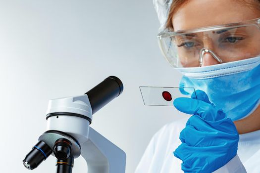 Woman scientist looking at slide with blood sample near microscope in laboratory