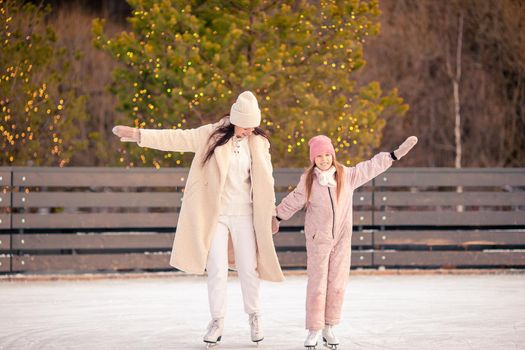 Little adorable girl with her mother skating on ice-rink