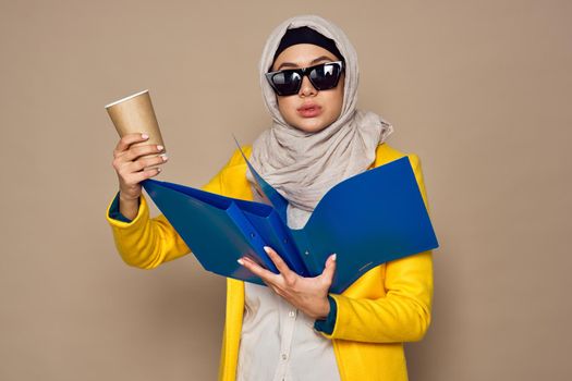 woman in sunglasses in hijab a cup of coffee beige background