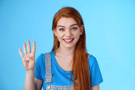 Cute carefree redhead female shopping, show four fingers, number fourth smiling lucky upbeat, amused positive expression, make order reservation table for friends, stand blue background